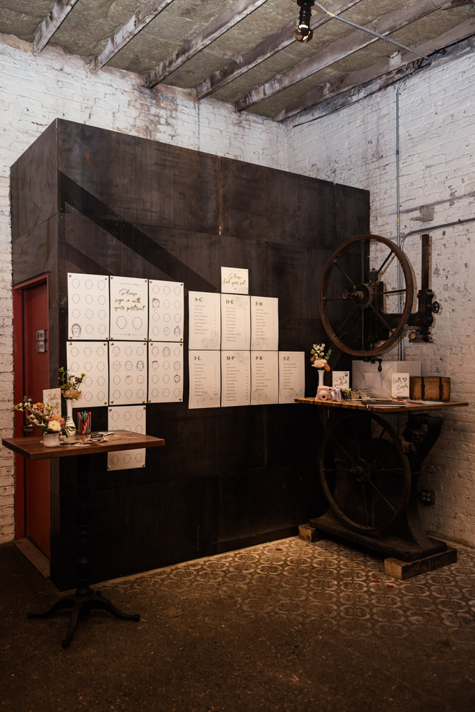 Guest seating chart and gcard and gift table in an industrial-themed space at The Joinery in Chicago with white brick walls and vintage machinery