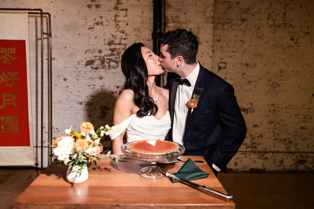 A bride and groom kiss after cutting their wedding cheesecake at The Joinery in Chicago