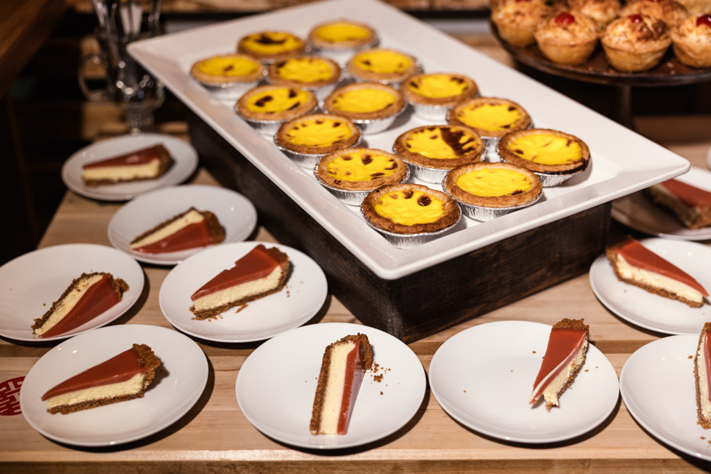 Detail photo of dessert table with slices of cheesecake and trays of egg tarts and other pastries on a wooden table for wedding reception at The Joinery in Chicago