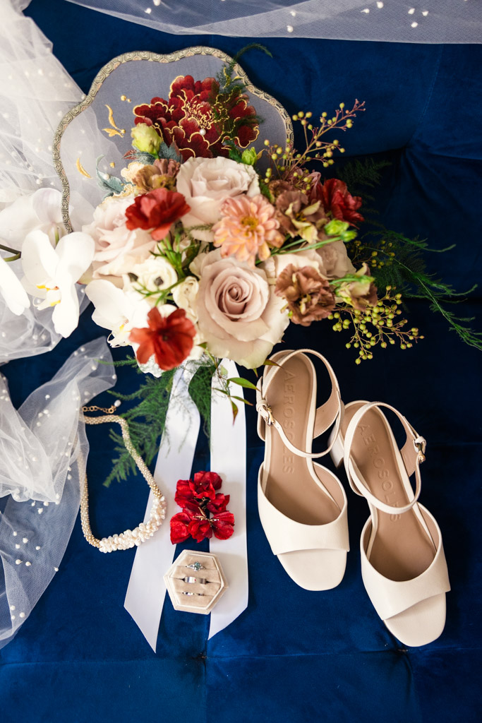 Bridal bouquet, white shoes, necklace, earrings, and veil arranged on a blue surface for wedding celebration at The Joinery in Chicago