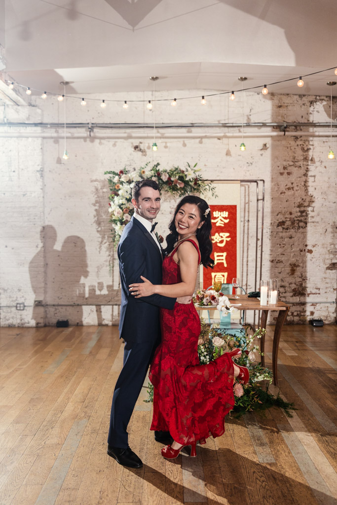 Portrait of newlywed couple during their first dance, surrounded by floral decorations and a red sign