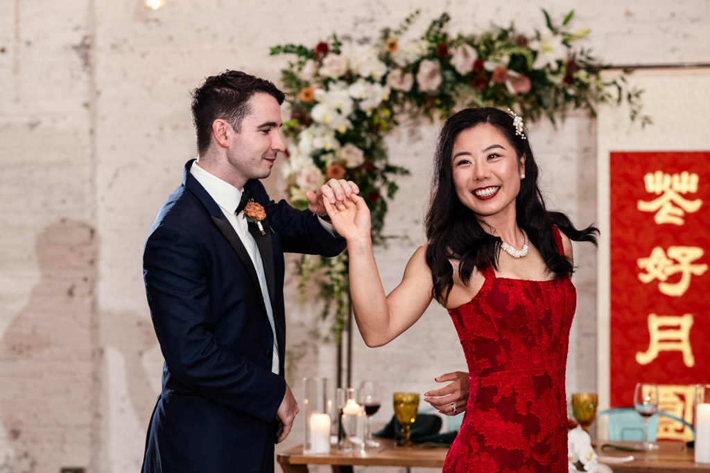 Bride in a red dress and groom in a tuxedo dance together at their wedding reception at The Joinery