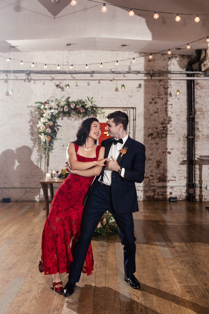 A couple dressed formally dance and smile together on joinery-crafted wooden floors in a beautifully decorated indoor venue.