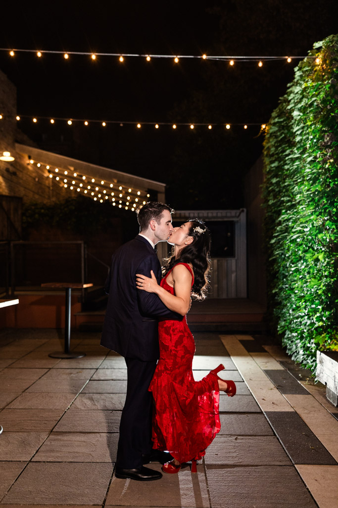 Bride and groom kiss under string lights on the patio at The Joinery at night