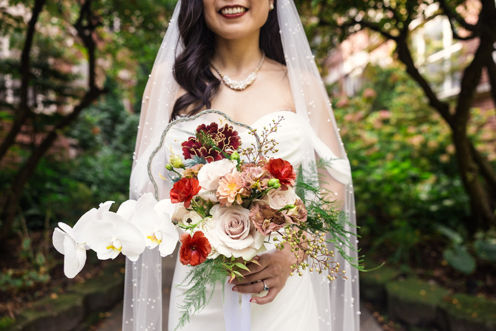Bride in a white dress holding a bouquet of red, white, and pink flowers before her wedding celebration at The Joinery in Chicago