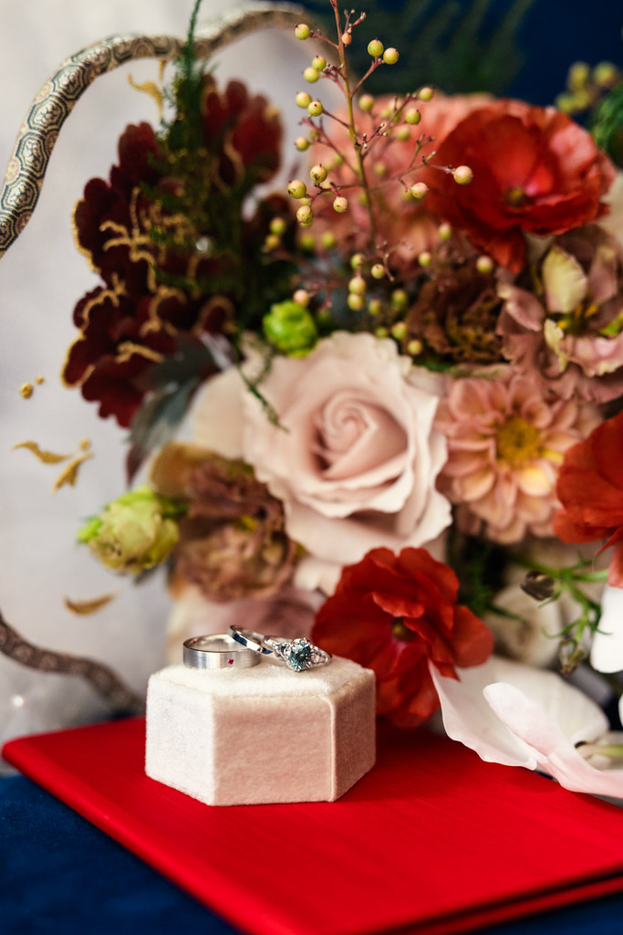 Wedding rings on a velvet box rest in front of a colorful floral bouquet and a red book for wedding celebration at The Joinery in Chicago