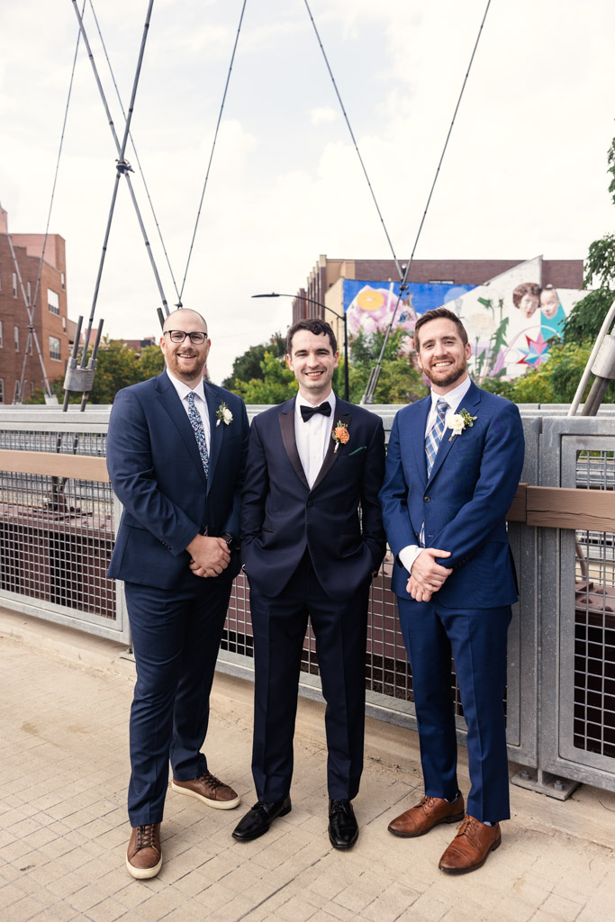 Groom and groomsmen stand smiling on the 606 Bridge in Wicker Park before wedding celebration at The Joinery in Chicago