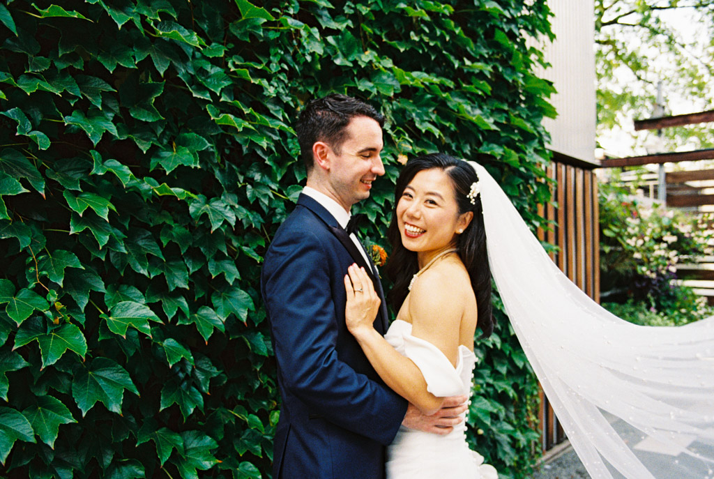 Bride and groom smiling and embracing in front of a leafy green wall outside The Joinery in Chicago