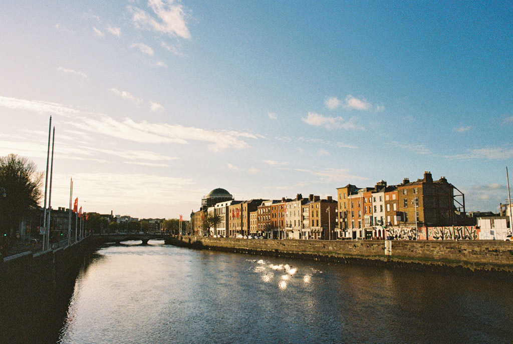 Film photo of the River Liffey flowing through Dublin with historic brick buildings beneath a blue sky with scattered clouds above