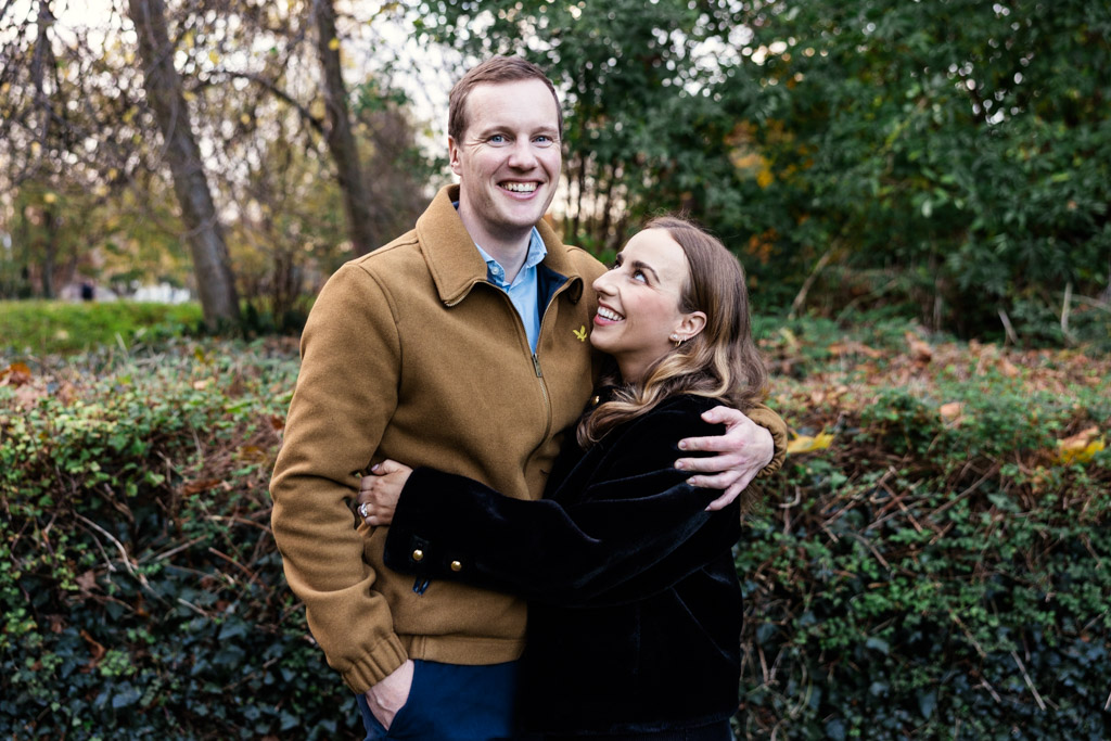 Portrait of happy engaged couple in front of green foliage and trees in Merrion Square, Dublin