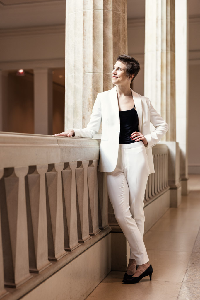 Emma Mullins in a white suit stands by a stone railing in the Art Institute of Chicago