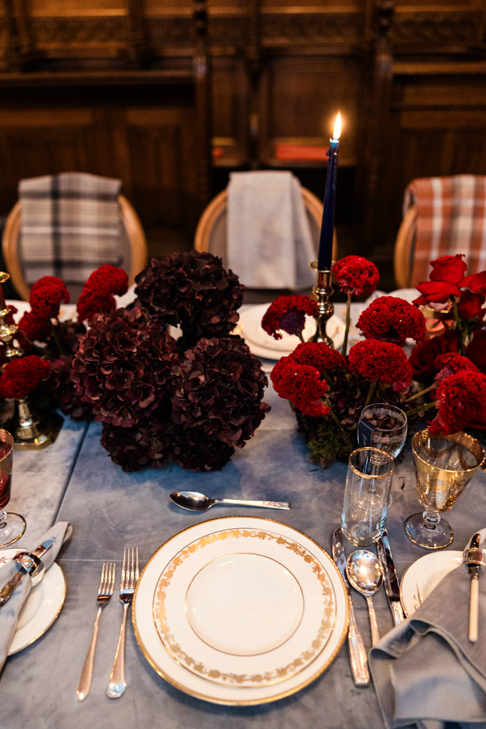 Guest table setting with gold-trimmed plates, red flowers, a blue candle, and plaid-covered chairs inside Markree Castle