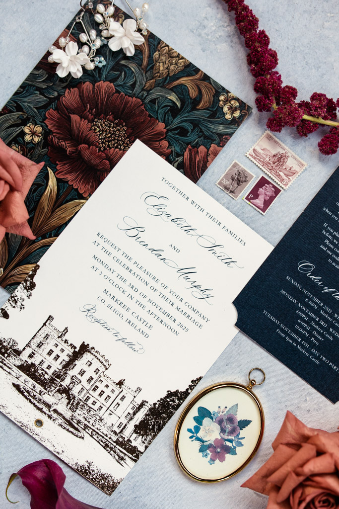 Floral wedding invitation suite with stamps, flowers, and an illustration of a castle on a textured blue surface for Markree Castle wedding celebration