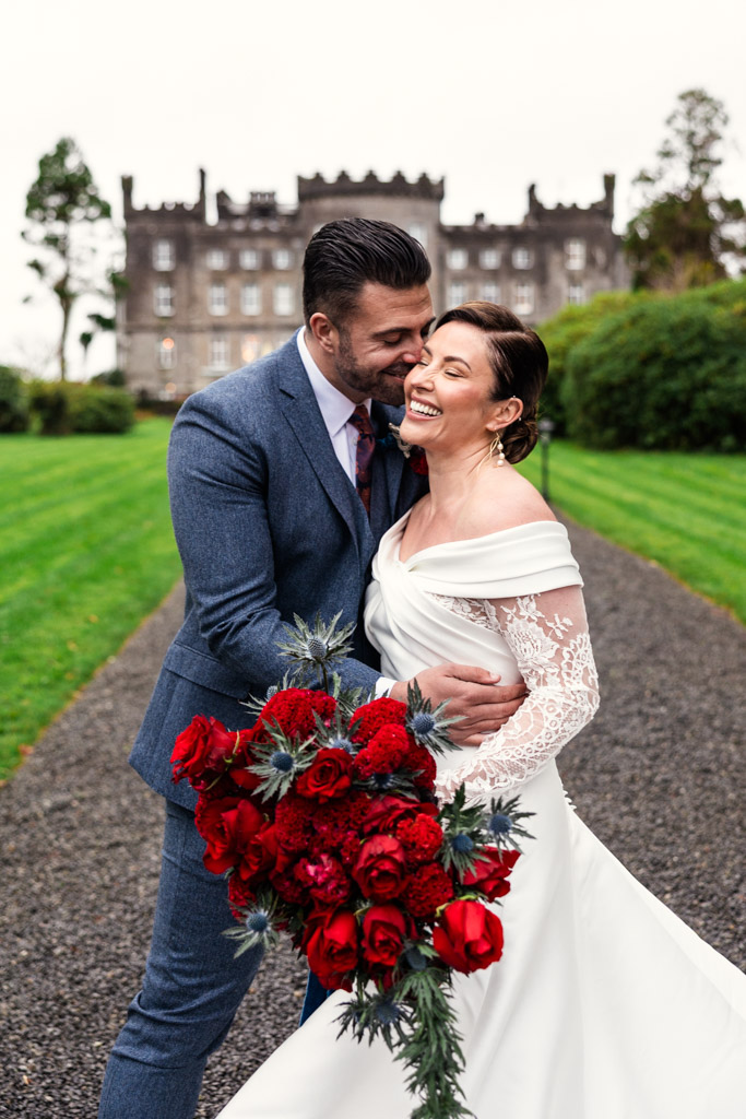 Candid photo of bride and groom embracing and smiling outside Markree Castle, the bride holding a bouquet of red roses