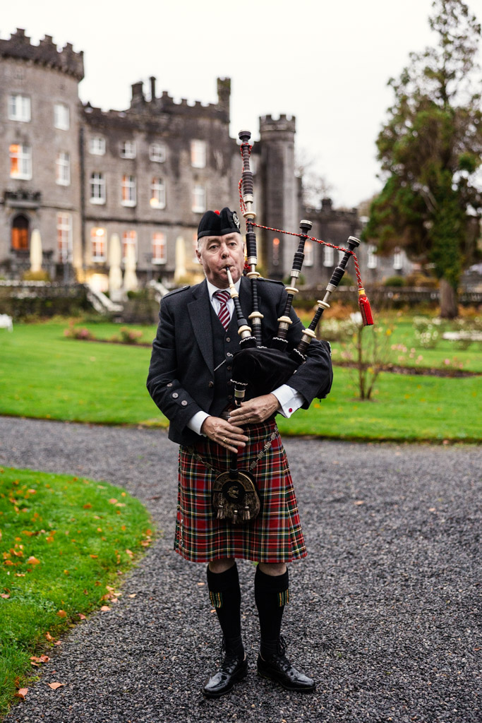 A man in traditional attire plays bagpipes outside Markree Castle on a cloudy day
