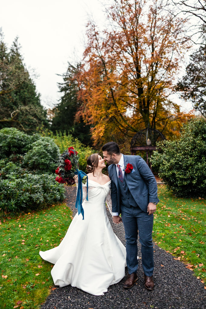 Bride and groom kiss outdoors on a garden path, surrounded by autumn trees and greenery on the grounds of Markree Castle