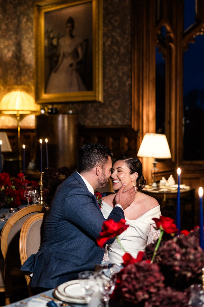 Bride and groom in formal attire smile at each other at a romantic, candlelit dinner table inside Markree Castle