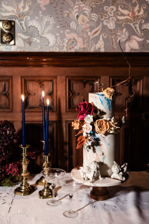 Tall marble-patterned cake with flowers beside two blue candles on a decorated table, perfect for an elegant Ireland wedding.