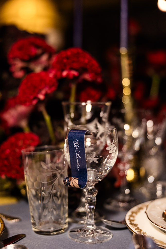 Guest table setting with etched glassware, red flowers, and a blue name tag on a wine glass for Markree Castle wedding celebration