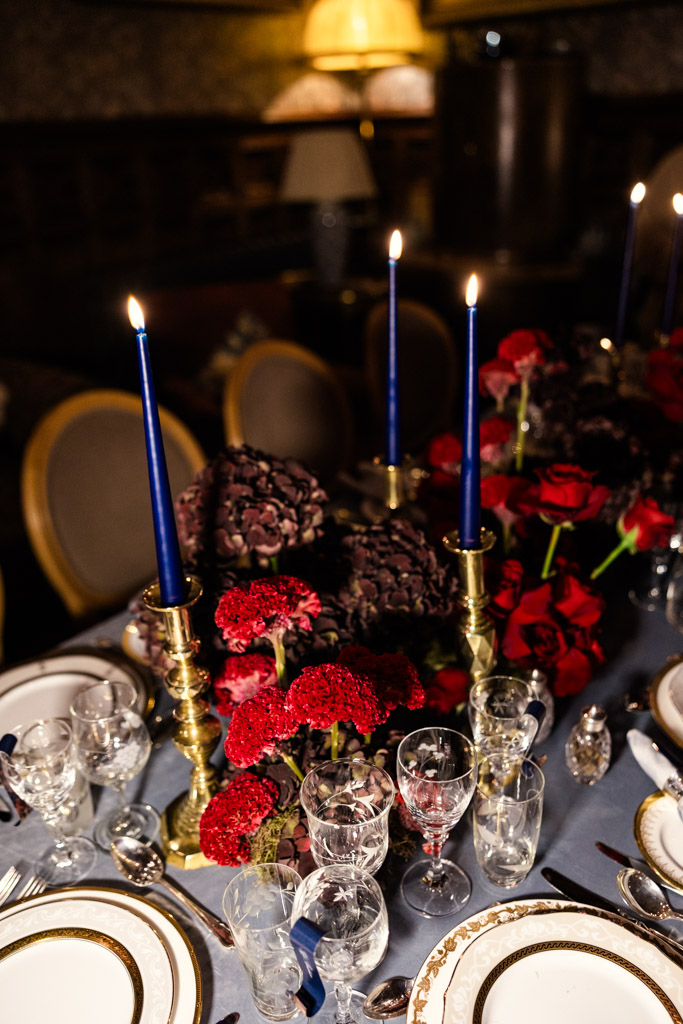 Guest table setting with blue candles, red flowers, gold accents, and glassware arranged for Markree Castle wedding dinner