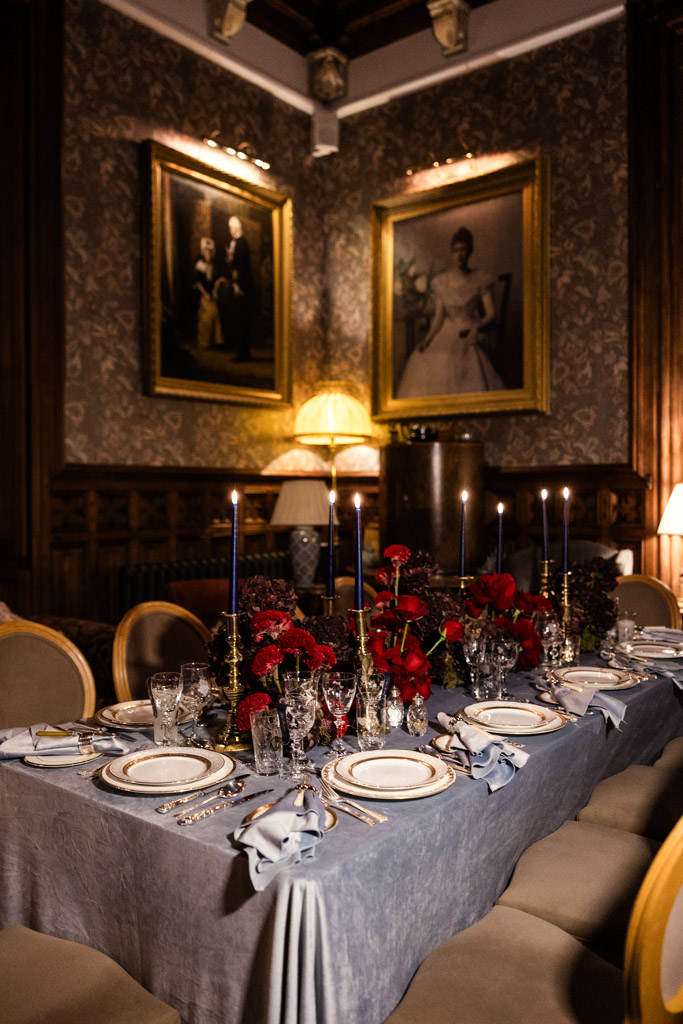 Guest dining table with red floral centerpiece, candles, and fine china in a vintage, art-filled room for Markree Castle wedding celebration