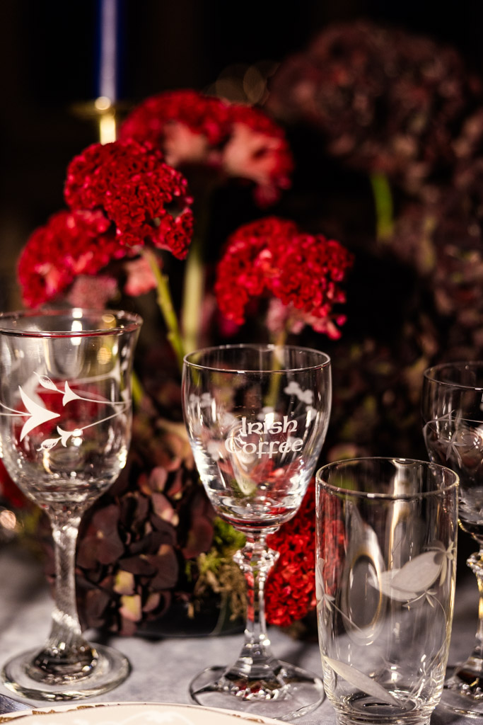 A close-up of assorted glassware on a table with red and dark purple flowers in the background for Markree Castle wedding celebration