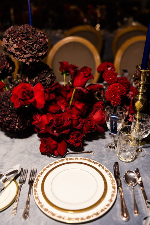 Elegant table setting with gold-trimmed plates and a red floral centerpiece, surrounded by cutlery and glasses—perfect for a romantic Ireland wedding celebration.