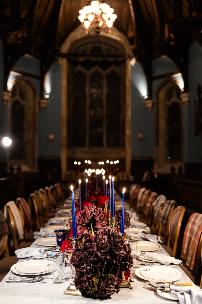 A long dining table set with blue candles, red flowers, and fine china in a grand hall inside Markree Castle