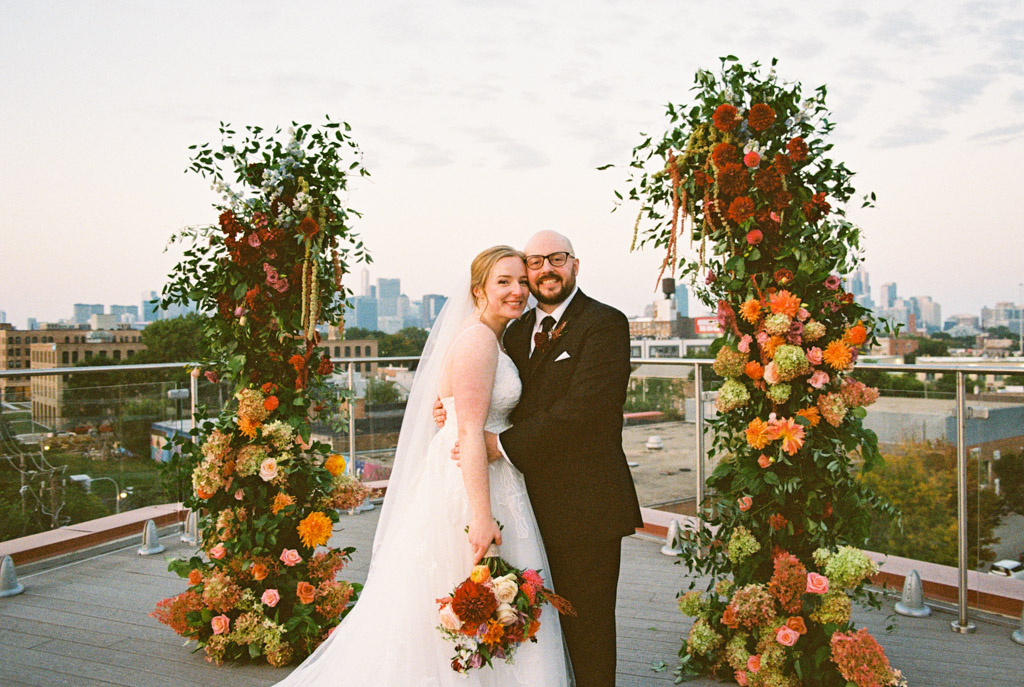 Film portrait of happy bride and groom embracing on the Lacuna Lofts rooftop, framed by floral arches with the Chicago skyline behind them