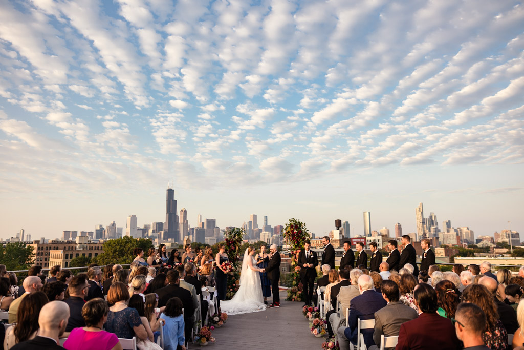 Outdoor rooftop wedding ceremony at Lacuna Lofts, featuring a stunning city skyline and dramatic clouds in the background