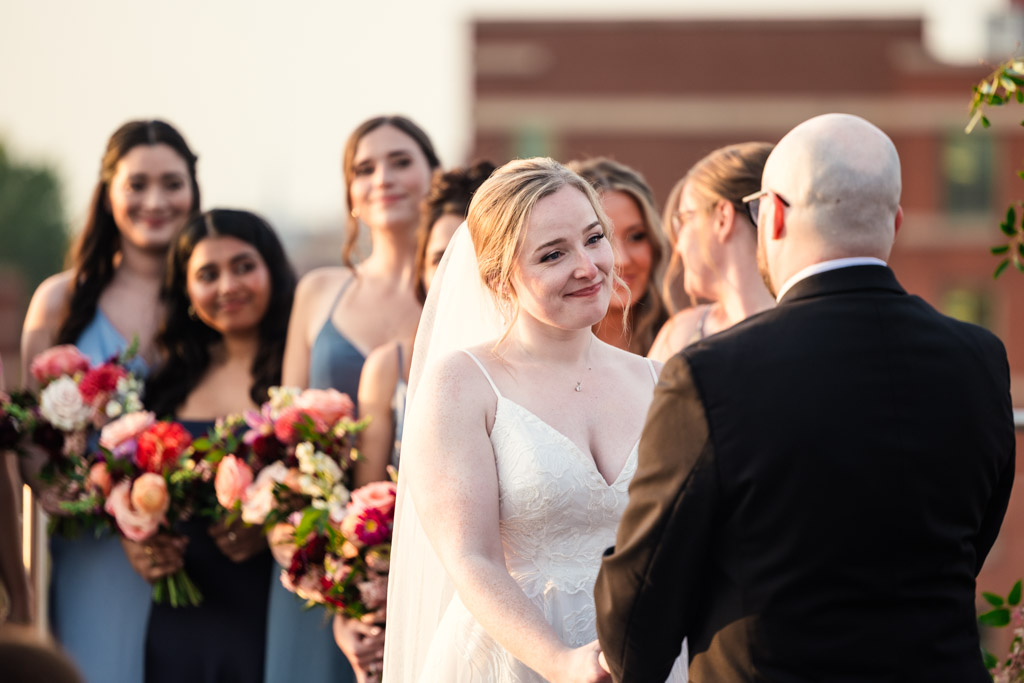 A bride and groom hold hands during their rooftop wedding ceremony at Lacuna Lofts, with bridesmaids holding bouquets behind them