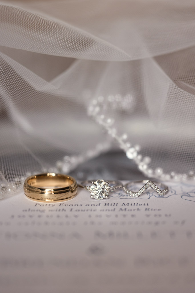 Gold wedding band and diamond rings on bride's veil with pearl details, resting on an invitation to wedding at Lacuna Lofts