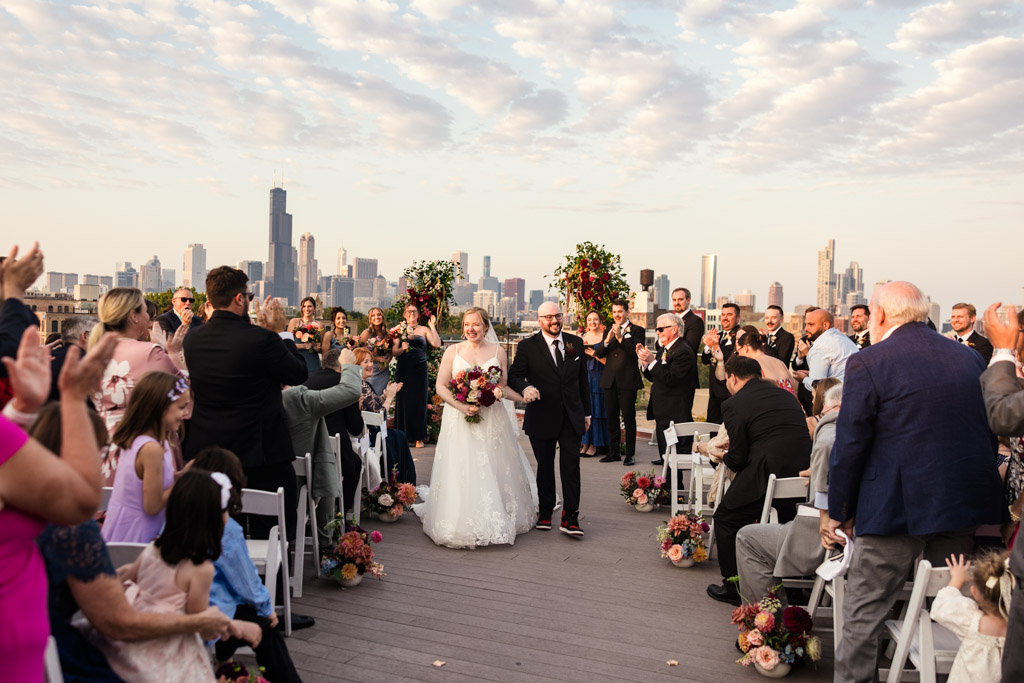 Bride and groom walk down the aisle after their rooftop wedding ceremony at Lacuna Lofts, guests applauding and the Chicago skyline in the background