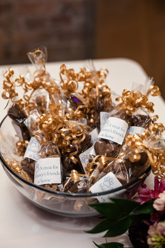 A glass bowl filled with treat bags tied with gold ribbon and labeled, 