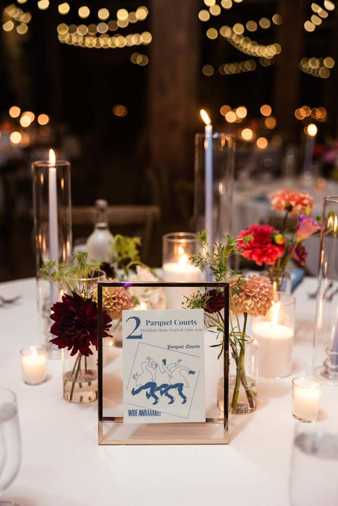 Guest table centerpiece with flowers, candles, and custom concert-themed table sign for wedding reception at Lacuna Lofts