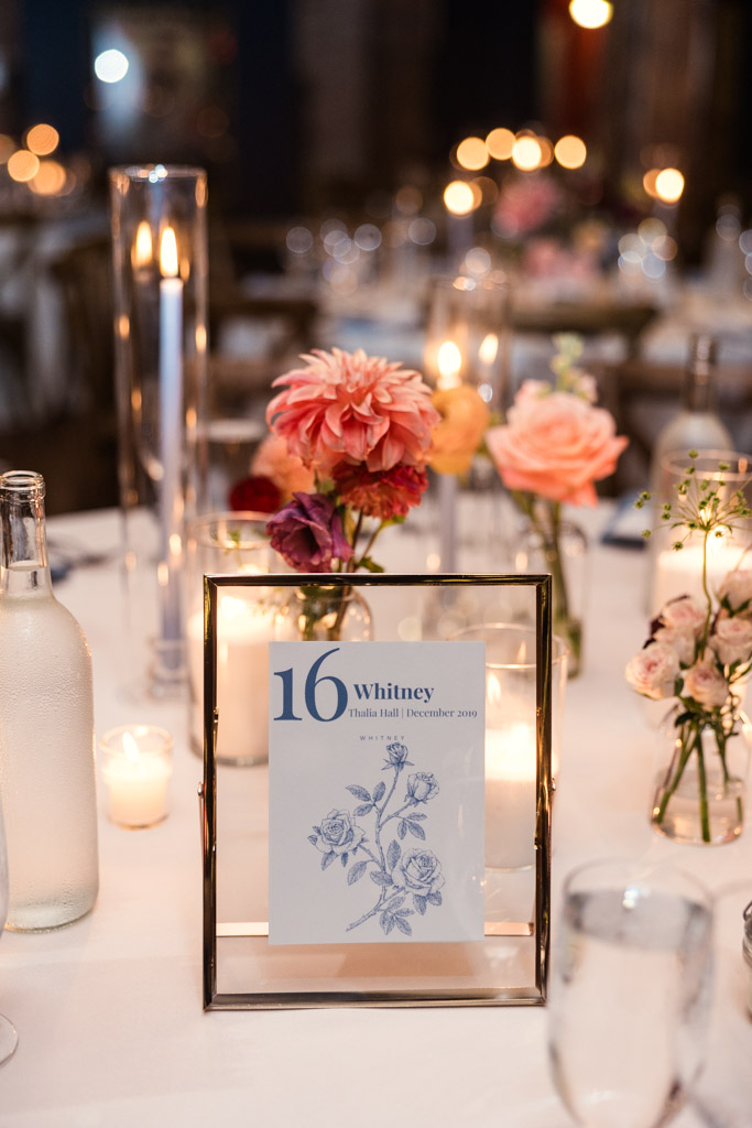 Guest table centerpiece with flowers, candles, and a framed concert-themed table sign for wedding reception at Lacuna Lofts