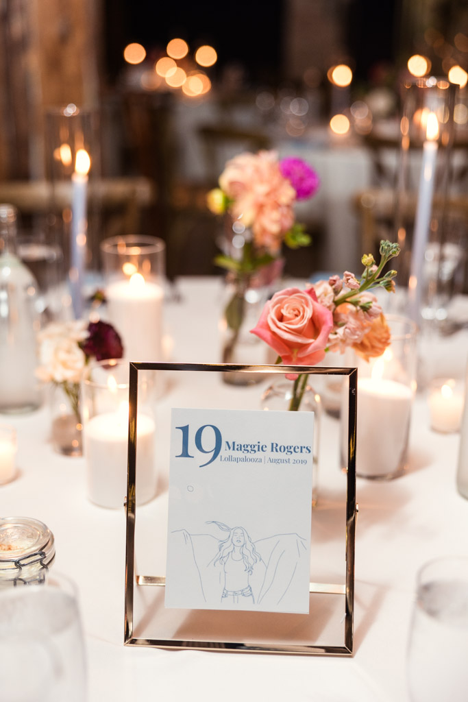 Guest table centerpiece with flowers, candles, and a custom concert-themed framed table sign for Lacuna Lofts wedding reception