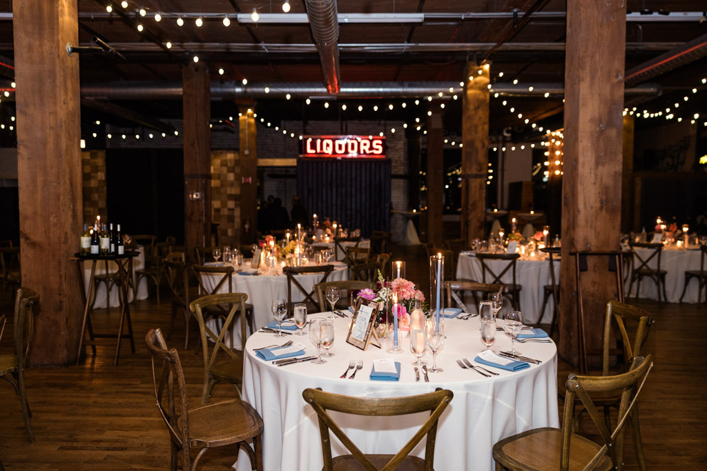 Guest tables set for wedding reception at Lacuna Lofts, with string lights and a glowing neon sign in the background