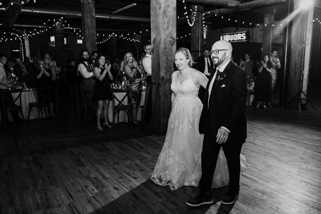 Black and white photo of newlywed couple entering their wedding reception at Lacuna Lofts as guests stand and applaud