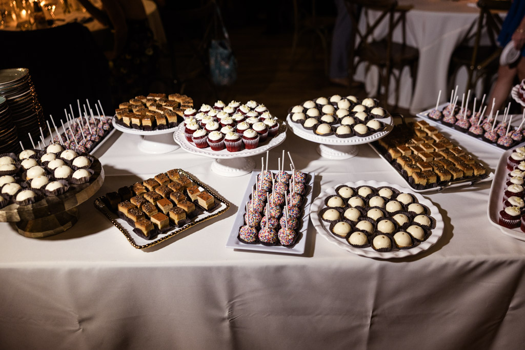 Dessert table at Lacuna Lofts wedding reception filled with assorted desserts, including cake pops, brownies, and cupcakes arranged on white platters