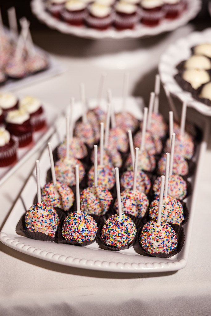 Tray of cake pops covered in rainbow sprinkles, arranged neatly with sticks upright on a white platter for wedding reception at Lacuna Lofts