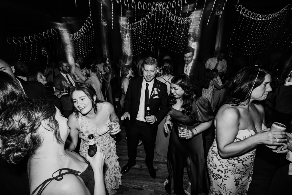Creative black and white photo of wedding reception guests dancing with string lights overhead at Lacuna Lofts