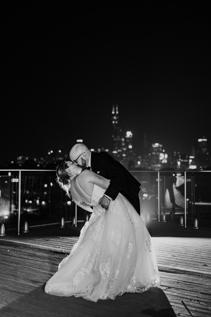 Romantic black and white photo of newlywed couple kissing at night on the rooftop of Lacuna Lofts, city lights glowing in the background