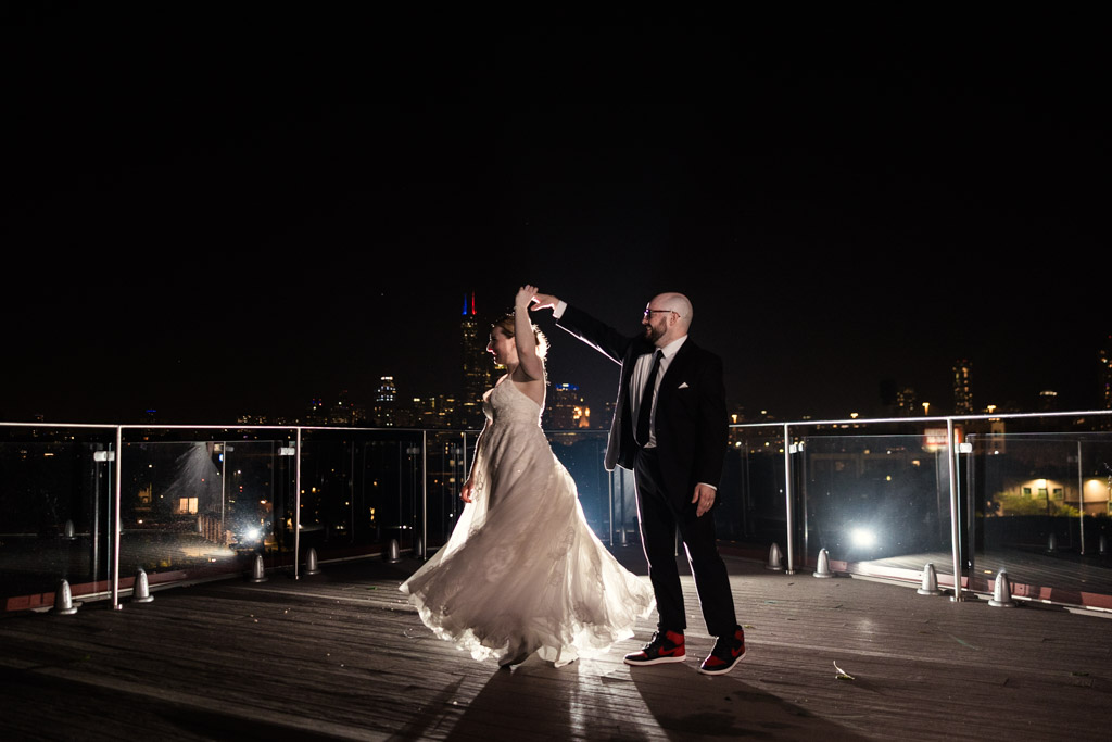 Bride and groom dance at night on the rooftop of Lacuna Lofts, with the Chicago skyline and bright lights shimmering in the background