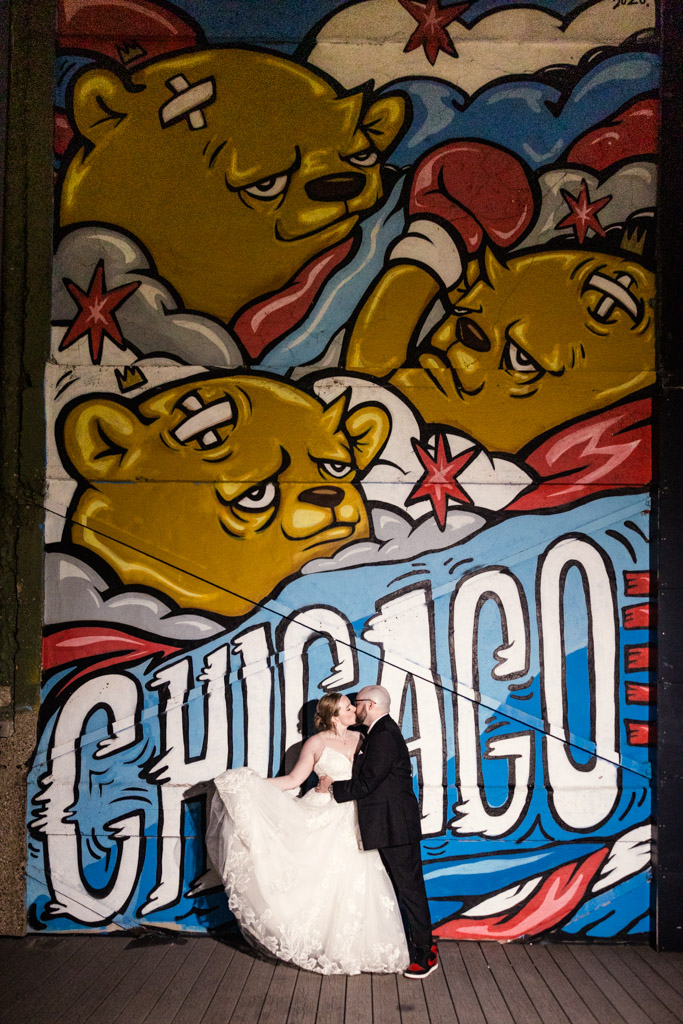 Bride and groom kiss in front of a colorful Chicago mural with cartoon bears and boxing gloves at Lacuna Lofts