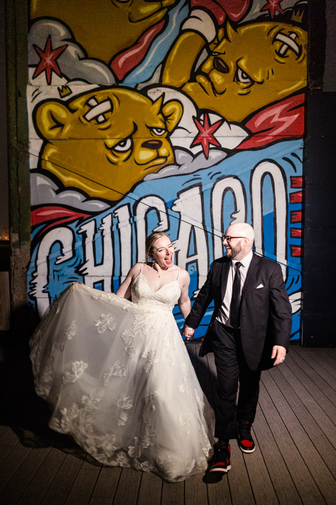 Joyful bride and groom walk in front of a vibrant Chicago mural with cartoon bear faces at Lacuna Lofts