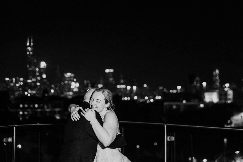 Black and white photo of bride and groom embracing joyfully on the Lacuna Lofts rooftop with the Chicago city skyline in the background