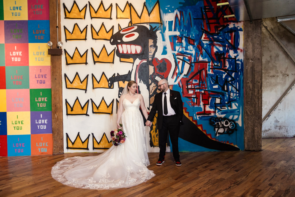 A bride and groom hold hands in front of a Basquiat-themed mural at Lacuna Lofts