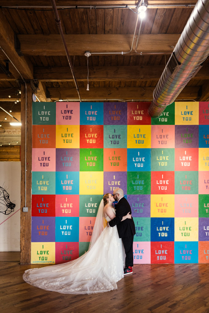 Bride and groom kiss in front of a colorful 
