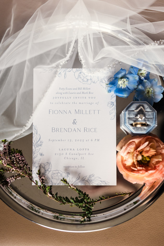 Wedding invitation on a silver tray with flowers, a ring box, veil, and pearl necklace nearby for wedding celebration at Lacuna Lofts